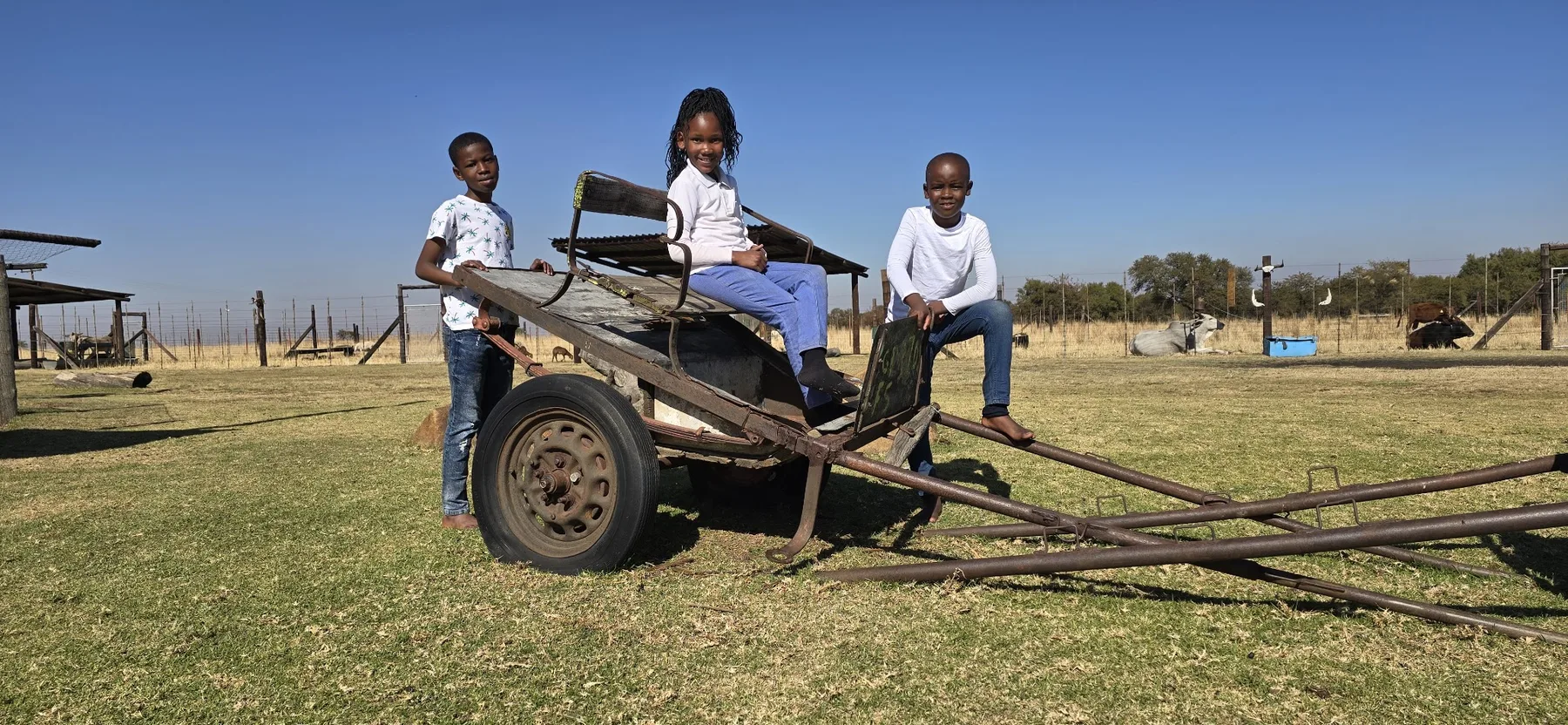 Three learners sitting on farm equipment under a wide Highveld sky