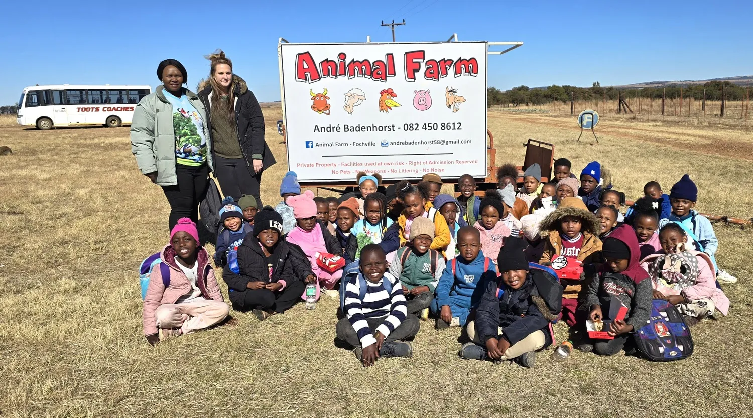 A school group photographed with their teachers in front of the Animal Farm sign, with their bus behind them